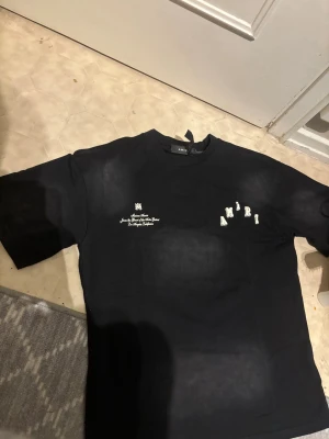 Svart t-shirt  - Svart t-shirt från Amiri med vit text och logga på bröstet. Klassisk rund halsringning och korta ärmar. T-shirten har en stilren design med tryckdetaljer och är tillverkad i mjuk bomull för en skön känsla.