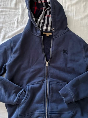 Marinblå hoodie från Burberry -  En riktigt snygg Marinblå burberry! Den är i jätte fin skick, den ar i storlek L men passar aven M! Inga solbrännor eller grova defekter kolla sista bilden där vi har ett litet håll som inte syns om man inte öppnar och börjar kolla riktigt noggrant + snörren ar borttappade annars ar detta en jätte fin tröja som sticker ut för det är inte så många som har denna färgen. Säljer denna för 620 priset kan eventuellt sankas vid snabb affär och köp direkt (. Kom inte med dumma priser🙂🙂)