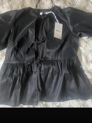 Svart glansig blus från NA-KD - Trendig svart blus från NA-KD i glansigt material med knytning framtill. Helt oanvänd säljer för fick hem 2 stycken ❣️