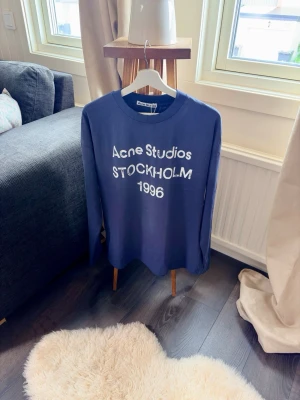  Longsleeve Acne Studios blue - Snygg blå långärmad t-shirt från Acne Studios med vit text 'Acne Studios STOCKHOLM 1996' på bröstet. Klassisk rund hals och avslappnad passform. Perfekt för dig som gillar streetwear och vill ha något stilrent men ändå trendigt. Aldrig använd, priset ej hugget i sten 🪨. Tveka inte att fråga vid minsta fundering! Skickar samma dag ! 🤝😁