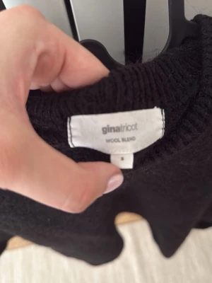 Svart stickad tröja Gina Tricot - Kortärmad svart stickad tröja från Gina Tricot i ullblandning. Tröjan har ribbad rund halsringning och en enkel, rak passform som passar perfekt till jeans eller kjol.