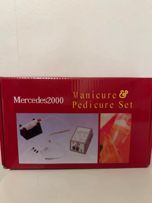 Mercedes2000 Manikyr & Pedikyr Set - Elektriskt manikyr- och pedikyrset från Mercedes2000. Innehåller maskin med sladd, flera sliphuvuden och hållare. Perfekt för nagelvård hemma. Maskinen är grå med svart och lila detaljer och har justerbar hastighet.