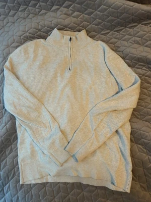  stickad tröja med halvzip - Säljer en beige stickad tröja från These Glory Days. Tröjan har halvzip, hög krage och är ribbstickad i mjukt material. Perfekt för lager på lager och enkel att matcha med jeans eller chinos.