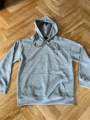 Grå hoodie från Polo Ralph Lauren - PRIS KAN DISKUTERAS!     Snygg grå hoodie från Polo Ralph Lauren med klassisk huva och dragsnören. Har en stor magficka och den ikoniska svarta loggan broderad på bröstet. Tillverkad i mjukt bomullsmaterial och har ribbade muddar vid ärmar och nederkant.