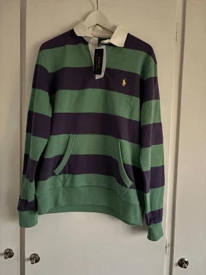 Randig rugbytröja från Polo Ralph Lauren - Säljer helt ny (tags kvar) randig rugby från Polo Ralph Lauren i storlek M. Tröjan har vit krage, lång ärm och klassisk gul broderad logga på bröstet. Tillverkad ibomull.  Nypris i butik är runt 2300:-.