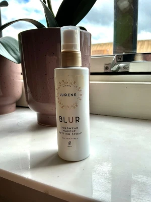 Lumene Blur Makeup Setting Spray - Fräsch setting spray från Lumene i vit plastflaska med guldfärgad spraypump. Produkten heter Blur Longwear Makeup Setting Spray och är vegansk samt passar alla hudtyper. Perfekt för att fixera sminket och ge en naturlig finish.