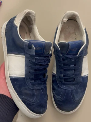 Blåa och vita sneakers från Valentino - Snygga sneakers från Valentino i mocka och läder. Skorna är blå med vita detaljer och har en klassisk låg siluett. Tjock vit sula och matchande blå skosnören. Perfekta för dig som vill ha en stilren och exklusiv look.