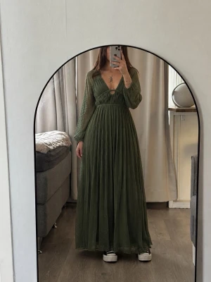 Långklänning med v-ringning ASOS Design - Khaki - Mörkgrön maxiklänning från ASOS i en elegant, romantisk modell med djup V-ringning, markerad midja och vackert plisserat fall. Transparanta prickiga ärmar och öppen rygg med knytning som ger en exklusiv och feminin kansla. Klänningen har ett mjukt, luftigt material som faller fint mot kroppen och rör sig vackert när man går. Perfekt till bröllop, sommarfest, middag, semester eller finare tillfallen. En otroligt fin statement-klänning som känns både lyxig, elegant och effortless. Skick: Helt ny 