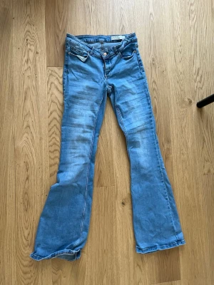 Blå bootcut jeans från vero moda  - Säljer ett par ljusblå bootcut jeans från vero moda med klassisk femficksdesign och utsvängda ben. Jeansen har slitningar framtill för en trendig look och är tillverkade i mjuk denim. Perfekta för dig som gillar retrostil och vill ha ett par bekväma jeans.