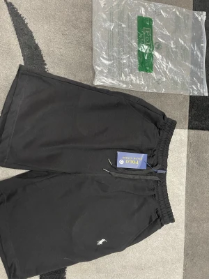 Svarta shorts från Polo Ralph Lauren - Svarta shorts från Polo Ralph Lauren med klassisk logga broderad framtill. Modellen har elastisk midja med snörning och är tillverkad i mjuk bomull. Perfekta för en avslappnad och stilren look.