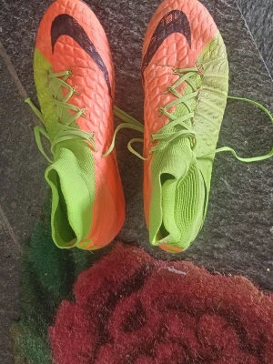 Nike Hypervenom fotbollsskor orange/grön - Säljer ett par Nike Hypervenom fotbollsskor i en riktigt snygg färgkombination av orange och neongrönt. Skorna har högt skaft, snörning och svart Nike-logga på ovansidan. Ovandelen är texturerad för bättre bollkontroll och materialet är syntetiskt.