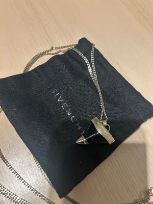 Givenchy halsband med svart/guld hajtand - Snyggt halsband från Givenchy med deras hajtand i svart och guldfärgad metall. Hänget har Givenchy-loggan ingraverad på gulddetaljen och kedjan är i matchande. Smal dubbelkedja. Säljes för ca 3000kr på Vestiaire. 
