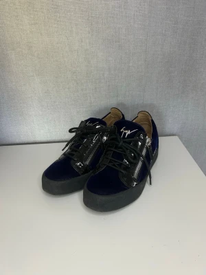 Blå Giuseppe Zanotti skor - Snygga sneakers i mörkblå sammet med svarta lackdetaljer och silverfärgade dragkedjor på sidorna. Skorna har svart sula, svarta skosnören och den ikoniska Zanotti-signaturen på plösen. Perfekt för dig som vill sticka ut med exklusiv stil.