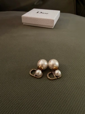 Dior örhängen med pärlor och strass - Snygga örhängen från Dior med vita pärlor i två storlekar, guldfärgade detaljer och glittrande strass på CD-loggan. Perfekt accessoar för dig som vill ha något extra till din look. Kommer i originalask. No original box.