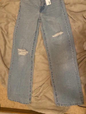 Ljusblå slitna jeans Boulevard XS - Säljer ett par ljusblå jeans från Boulevard i storlek XS. Jeansen har raka ben och slitna detaljer på båda benen för en trendig look. Perfekta för dig som gillar en avslappnad och modern stil. Materialet är klassisk denim.