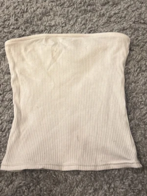 Tubtopp - Tub topp / bandeau topp, ribbad vit i fint skick men tyvärr en liten fläck men den är ganska ljus och inte jätte synlig☺️ tänker att de  kanske går att vända på den om man stör sig på de