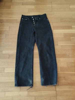 Hope Criss - Säljer ett par svarta jeans med vida/raka ben. Jeansen har råa, fransiga benslut och knäppning med knappar framtill. Klassisk femficksmodell i kraftig denim, perfekt för en avslappnad och trendig look. W28 L32