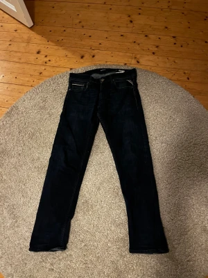 Mörkblå jeans från Replay - Säljer ett par mörkblå jeans från Replay med klassisk femficksmodell och raka ben. Jeansen har en snygg tvätt och detaljer som kontrastsömmar samt Replay-lapp bak i midjan. Perfekta för dig som gillar stilrena och tidlösa jeans.