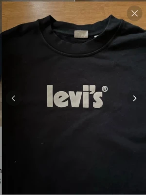 Svart sweatshirt från Levi's - Klassisk svart sweatshirt från Levi's med stort vitt logotryck på bröstet. Tröjan har rund halsringning, långa ärmar och ribbade muddar vid ärmslut och nederkant. Perfekt för en avslappnad och stilren look.