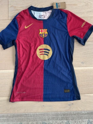 FC Barcelona matchtröja Raphinha - Snygg FC Barcelona matchtröja från Nike i rött och blått med guldfärgade detaljer. Tröjan har klubbmärke, Spotify-logga och nummer 11 med Raphinha på ryggen. Tillverkad i lätt och ventilerande material, perfekt för fotbollsträning eller match.