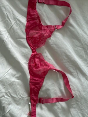 Rosa spets-bh från Hunkemöller - Säljer en snygg rosa bh från Hunkemöller med tunna axelband och vacker spetsdetalj över kuporna. Bh:n har justerbara band och en feminin design som ger ett lyxigt intryck. Perfekt för dig som gillar färg och fina detaljer. Jag har aldrig använt den 