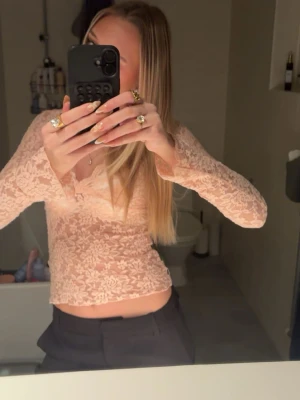 Rosa spetsblus med v-ringning - Säljer en rosa, långärmad spetsblus med v-ringning och blommigt mönster. Toppen är croppad och har en feminin, figurnära passform som ger en snygg siluett. Perfekt att styla med både jeans och kjol.