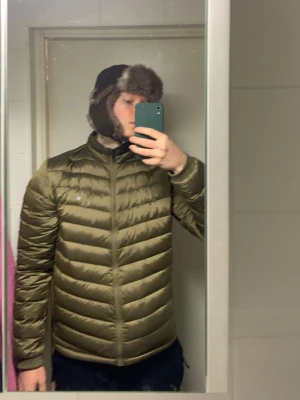 Olivgrön dunjacka gant  - Snygg olivgrön dunjacka med huva och quiltad design. Jackan har dragkedja framtill, ribbade muddar vid ärmslut och en diskret logga på bröstet. Perfekt för kalla vinterdagar och riktigt skön att bära tack vare lättviktigt material. Jackan har jag använt i ett år! Skick enligt bilder. Den har vissa små områden som har mörknad men inget som märks av! Säljs pågrund att jag har tröttnat på den.