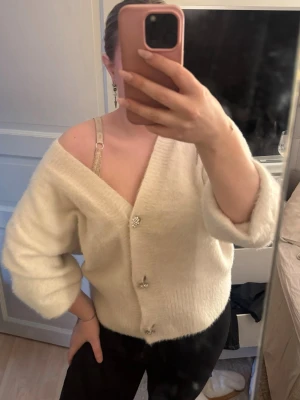 Vit fluffig kofta med pärlknappar - Mysig vit kofta med fluffig känsla och v-ringning. Koftan har tre dekorativa pärlknappar framtill. Jag brukar vika upp ärmarna (se bild 1) men jättefin annars också💗