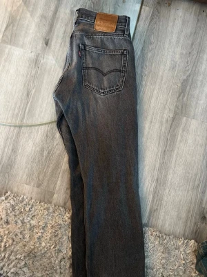 Levi's jeans  - Säljer ett par klassiska svarta Levi's jeans med rak passform och fem fickor. Jeansen har en snygg tvättad look, läderpatch bak i midjan och den ikoniska röda Levi's-taggen på bakfickan. Perfekta för en avslappnad och trendig stil.