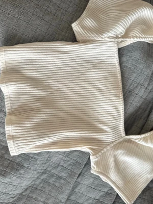 Vit ribbad offshoulder topp - Trendig vit ribbad topp med offshoulder-design och korta ärmar. Toppen har en croppad passform och är tillverkad i ett mjukt, stretchigt material som sitter snyggt på kroppen. Perfekt att styla med höga jeans eller kjol. Säljer då den knappt är använd