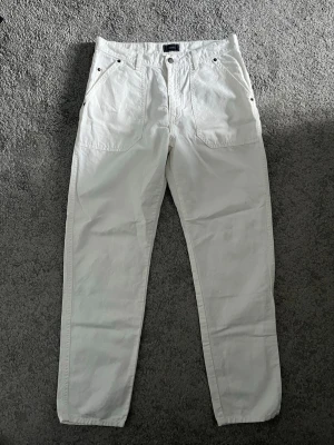 Vita raka jeans från boomerang  - Säljer ett par vita jeans med raka ben och stora framfickor. Jeansen har en avslappnad passform och silverfärgade nitar vid fickorna. Perfekta för en clean och stilren look. Materialet känns som bomull och de har klassisk midja.