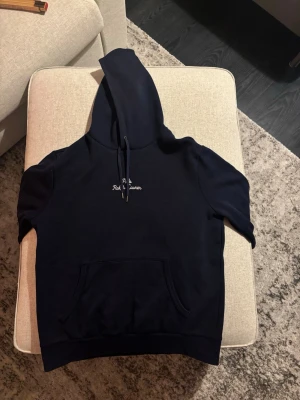 Mörkblå hoodie från Polo Ralph Lauren - Snygg mörkblå hoodie från Polo Ralph Lauren med broderad logga på bröstet i vit text. Klassisk känguruficka framtill och justerbar dragsko i huvan. Perfekt för en avslappnad och stilren look. Tillverkad i mjukt bomullsmaterial. Storlek M, men passar även S. Org. pris 2395kr