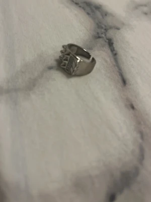 Silvrig ring med rutmönster - Unik silvrig ring i metall med ett coolt rutmönster och små spikes  runt om. Ringen har en bred design och sticker verkligen ut på fingret. Perfekt för dig som gillar statement-smycken och även justerbar där bak 