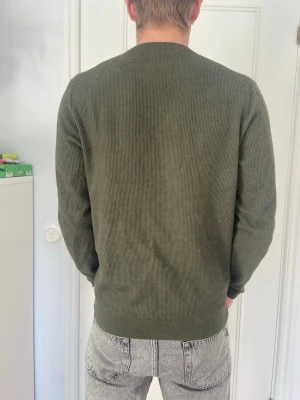 Olivgrön stickad tröja unisex - Säljer en stilren olivgrön stickad tröja från Mango med rund hals och ribbade muddar. Knappt använd Normal i storleken 