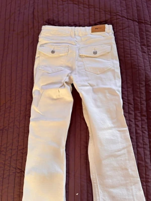 Vita bootcut jeans från Gina Tricot - Säljer ett par vita jeans från Gina Tricot med bootcut-modell. Jeansen har två bakfickor med lock och knappdetaljer samt bälteshällor. Materialet är stretchigt denim som sitter snyggt och bekvämt. Inge tecken på användning!