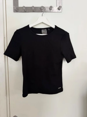 Svart t-shirt från Esprit - En klassisk svart t-shirt från Esprit med rund hals och korta ärmar. T-shirten har en enkel och stilren design, perfekt att matcha med jeans eller kjol. Tillverkad i mjuk bomull för skön komfort.