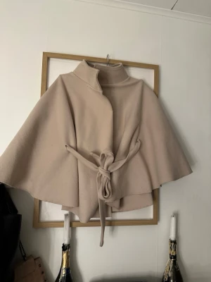 Beige poncho - Begie ponsho ifrån Missay, den guldiga knappen har låssnas, ingenting som sticker ut, å den brhövs inte, (kan byta imot svart)