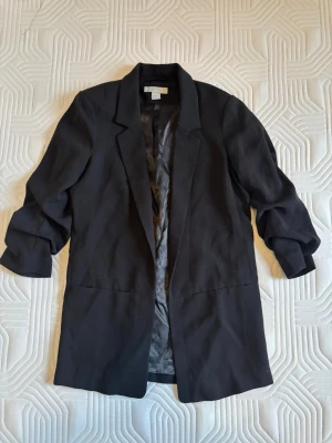 Svart Kavaj H&M - Stilren svart oversized kavaj med klassisk krage och ”scrunchad” trekvarts-ärmar. Kavajen har slät yta och är helfodrad på insidan. 