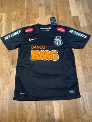 Santos 11/12 away kit X Neymar jr #11 - Säljer en svart Santos FC matchtröja från Nike med Neymar Jr och nummer 11 på ryggen. Tröjan har flera sponsorloggor, klubbmärke på bröstet och är tillverkad i lätt, andasvänligt material. Perfekt för dig som älskar fotboll och vill ha en ikonisk supportertröja.