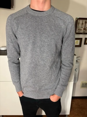 Grå stickad tröja, SELECTED - En enkel och stilren grå stickad tröja med rund hals och långa ärmar. Tröjan har ribbade muddar vid ärmslut och nederkant, perfekt för lager på lager. Passar till det mesta och är ett måste i garderoben.