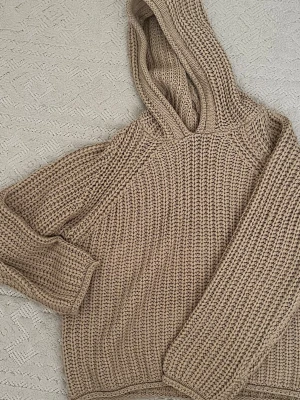 Beige stickad hoodie från Noisy May - Stickad hoodie i beige från Noisy May med grovstickad struktur och avslappnad passform. Tröjan har huva och långa ärmar, perfekt för lager på lager och en chill look. Materialet känns mjukt och mysigt, och färgen är lätt att matcha till det mesta.