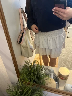 Vit volangkjol med resårmidja - Söt vit kortkjol med volanger och bred resår i midjan. Kjolen har en luftig och lätt känsla, perfekt för varmare dagar. Enkel att matcha med olika toppar för en trendig look.