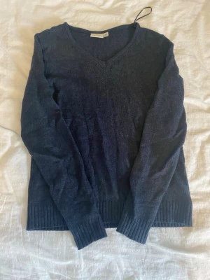 Mörkblå stickad v-ringad tröja från Vila - Snygg mörkblå stickad tröja från Vila med v-ringning och långa ärmar. Tröjan har ribbstickade muddar vid ärmslut och nederkant. Använd ett par gånger, lite nopprig.