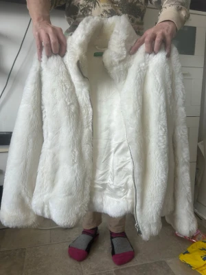 Vit fuskpälsjacka med dragkedja - Säljer en fluffig vit fuskpälsjacka med hög krage och dragkedja framtill. Jackan har en mjuk, silkeslen insida och en klassisk rak passform. Perfekt för att hålla värmen under kalla dagar och ger en trendig look.