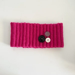 Virkad rosa öronvärmare  - Gullig rosa handvirkad öronvärmare perfekt för vintern! Dekorerad med knappar framtill. Mått: Bredd: 22cm Längd: 9,5cm💕 Skriv om ni har fler frågor!
