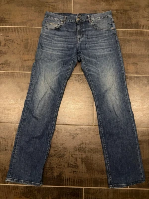 Mörkblå raka jeans från BOSS - Snygga mörkblå jeans från BOSS med klassisk femficksmodell och raka ben. Jeansen har en diskret tvättad look och metallknappar. Perfekta för dig som gillar stilrena och tidlösa jeans i ett mjukt denimtyg. Storlek 33/32