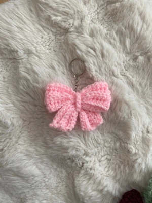 Rosa virkad nyckelring  - Supersöt rosa hårrosett i virkat garn med metallring för enkel fastsättning i håret eller på väskan. Rosetten är fluffig och har en klassisk form som ger en gullig touch till din look. Perfekt accessoar för dig som vill sticka ut lite extra.