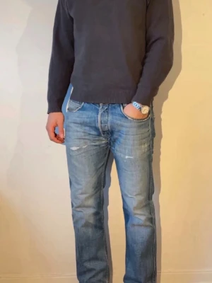 Blå raka jeans med slitningar - Säljer ett par blå jeans med raka ben och snygga slitningar framtill. Jeansen har klassisk femficksdesign och ljus tvätt med lite blekta partier. Perfekta för en avslappnad och trendig look.