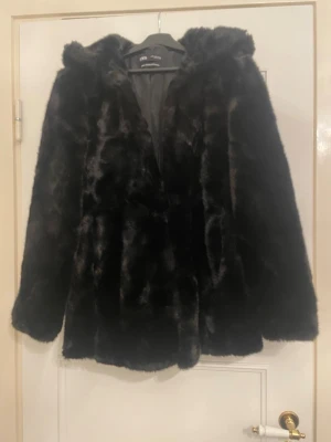 Svart fejkpälsjacka från Zara, storlek S - Svart fejkpälsjacka från Zara, storlek S. Aldrig använd. Luva och lätt A-linjeformad. Stängs med små hakar.