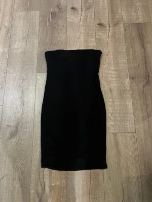 Svart axelbandslös klänning Forever 21 - Säljer en svart, axelbandslös klänning från Forever 21. Klänningen är figurnära och har en enkel, stilren design som slutar ovanför knäna. Perfekt för dig som gillar minimalistisk stil och vill ha en klassisk svart klänning i garderoben.